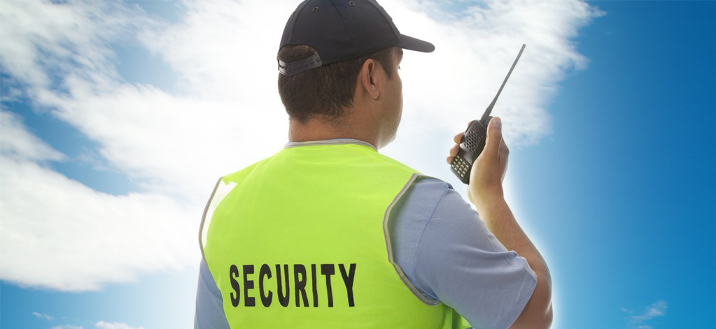 Security guard using a walkie-talkie outdoors.